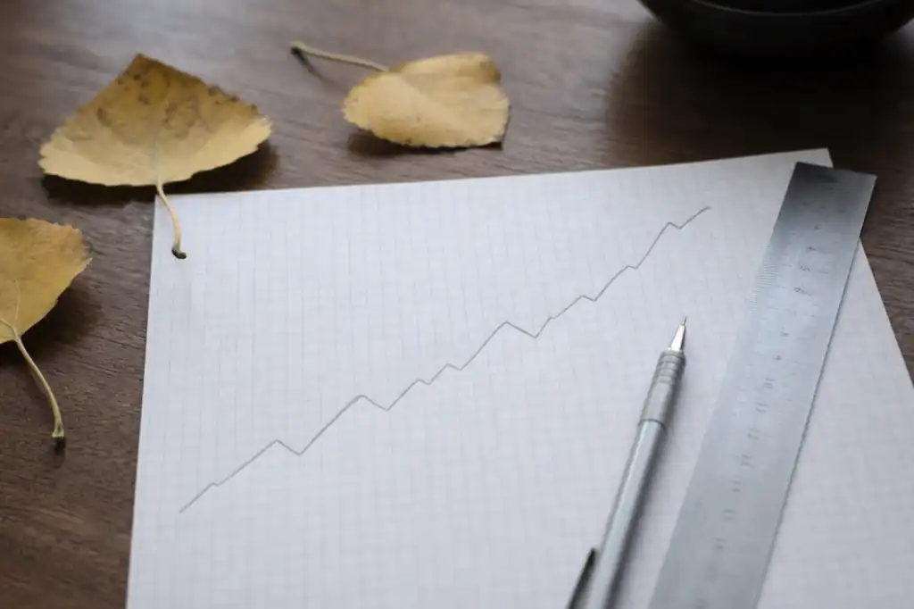Graph paper with a rising pencil line, a steel ruler and aspen leaves on a desk